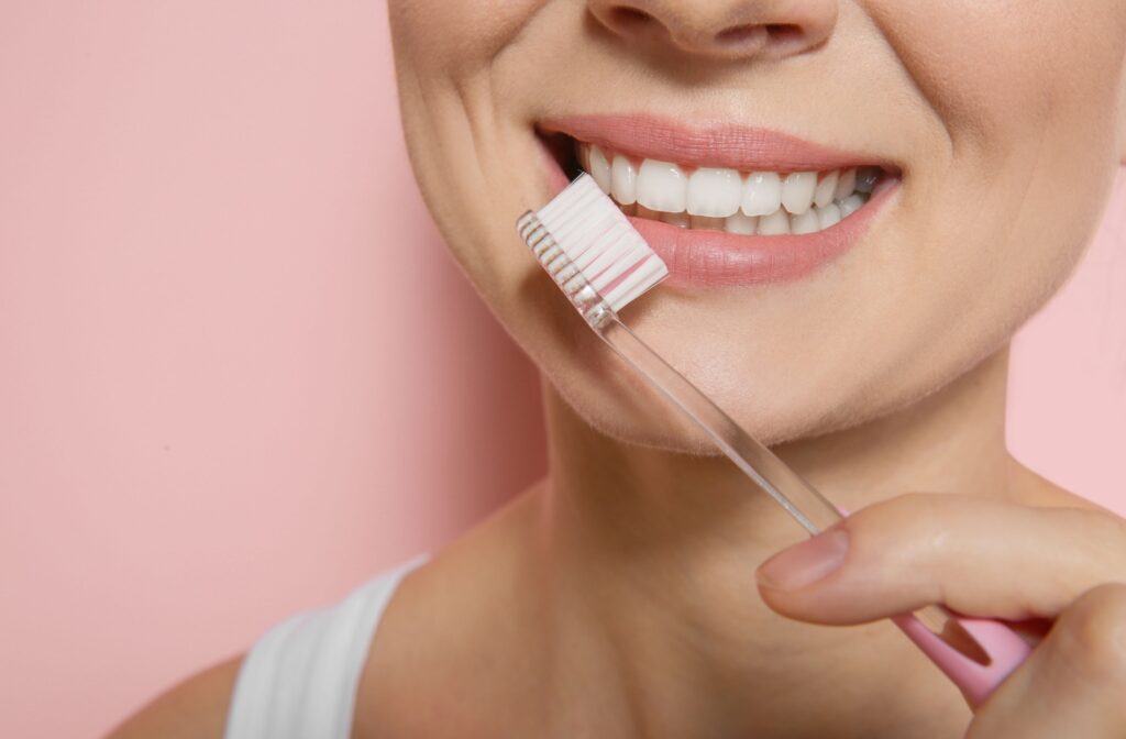 A smiling adult with a bright smile holds a toothbrush in front of their teeth.