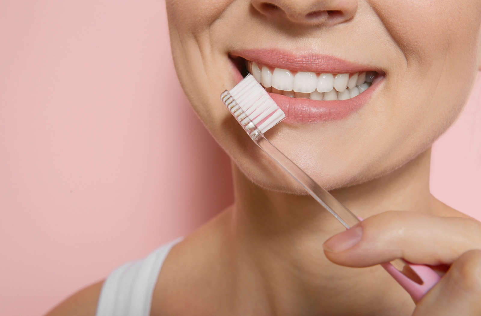 A smiling adult with a bright smile holds a toothbrush in front of their teeth.