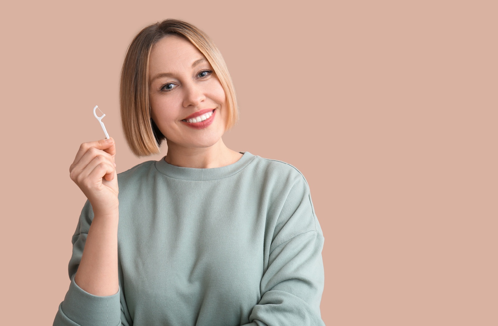 Someone holds a floss stick with a smile, having no issues after learning how to floss properly.