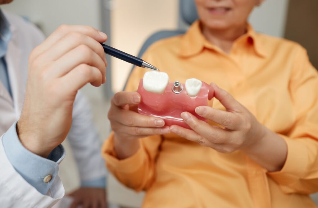 A patient's hands holding a dental plant model while their dentist explains the procedure.